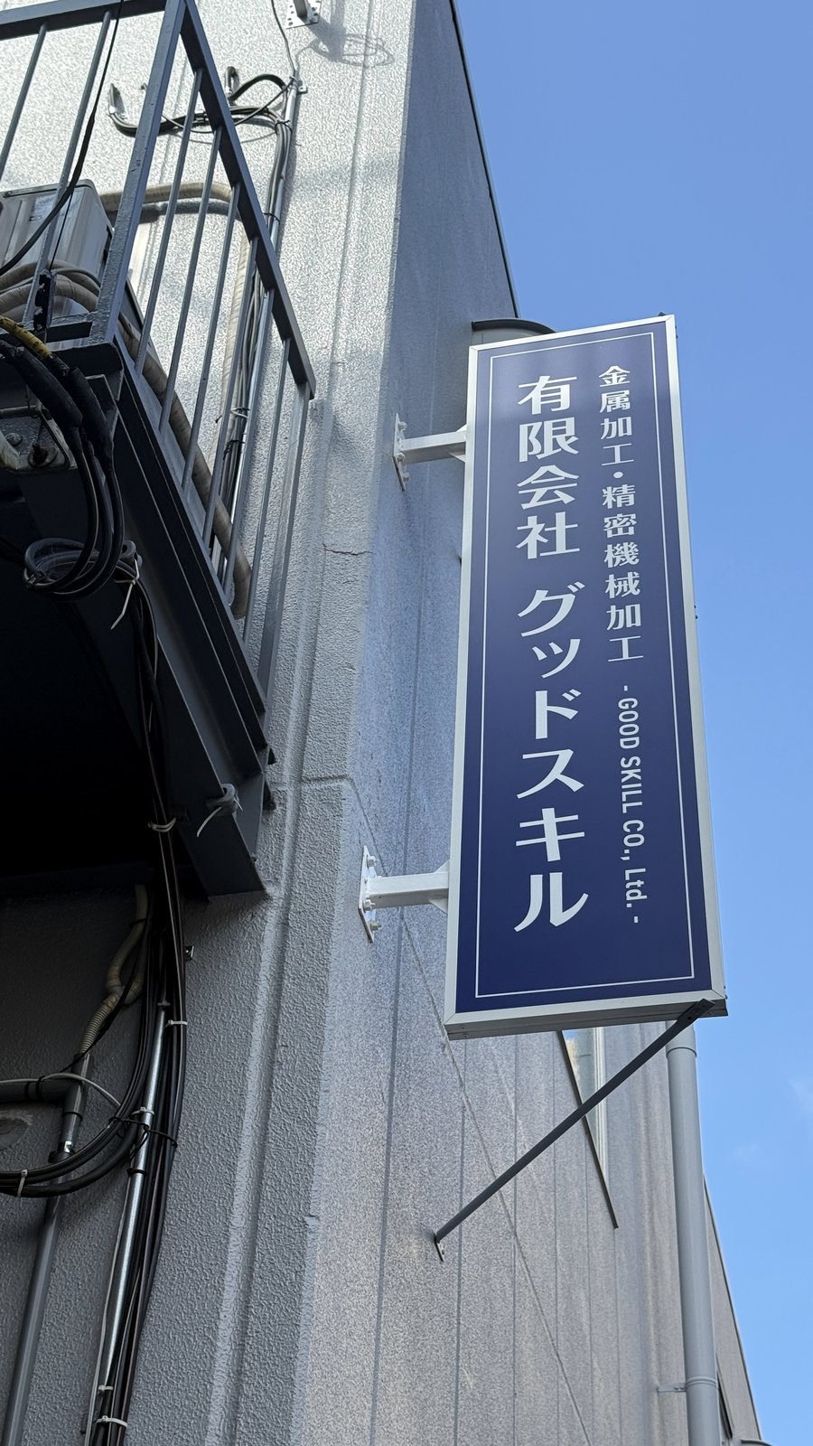 工場外壁に掲げられた有限会社グッドスキルの縦型社名看板