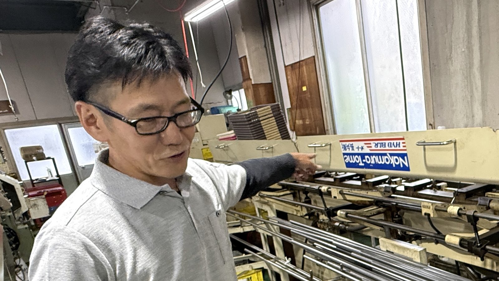 金属の丸棒材料が並ぶ工場内に立つグッドスキルの代表者