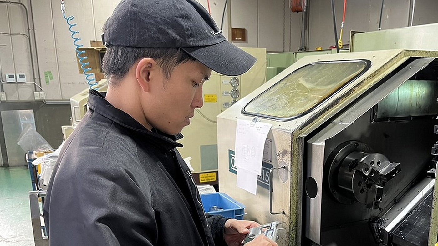 NC旋盤の前で加工品の寸法を測る製造スタッフ