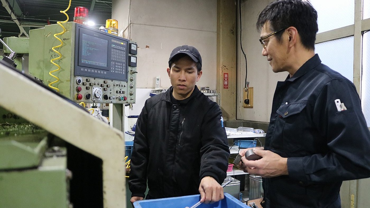 工場のNC旋盤の前で加工品を確認する2名の製造スタッフ